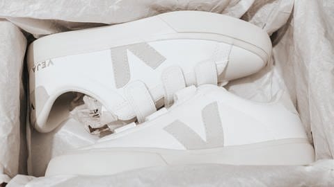 In einem Schuhkarton liegen ein Paar weiße Sneaker von der nachhaltigen Marke Veja. Die nachhaltigen Sneaker haben ein graues Veja-Logo an der Seite