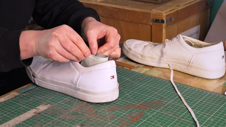 Ein Stück dünnes Leder wird von der Besitzerin einer Schuhreparatur-Werkstatt an den Fersenteil eines Sneakers geklebt.