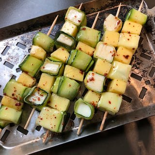 Zucchini-Mango-Spieße mit Chiliflocken liegen auf einer Edelstahlplatte