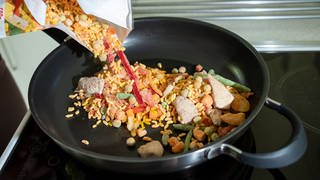 Tiefkühl-Paella wird in eine Pfanne geschüttet