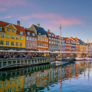 Man sieht Nyhavn in Kopenhagen mit bunter Häuserfassade und einem rot-weißen Boot.