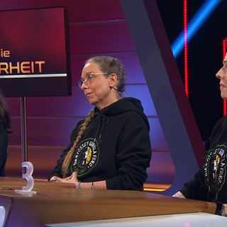 Drei Frauen in schwarzen Hoodies sitzen am Sag die Wahrheit Pult