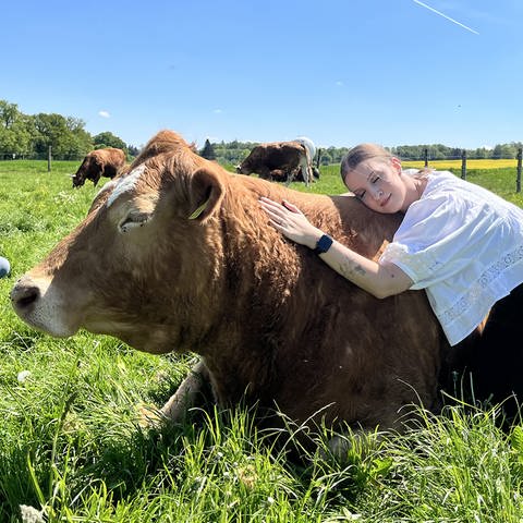 Junge Frau kuschelt mit Kuh auf einer Wiese