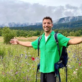 Treffpunkt Moderator Ramon Babazadeh steht vor einer Wiese mit Bergen in Tschechien