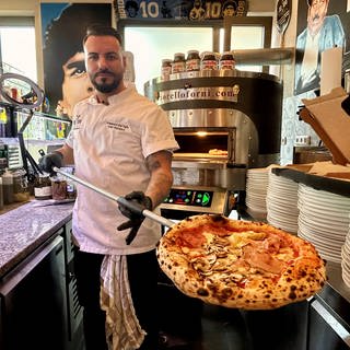 Pizzabäcker Francesco del Tufo hält eine frisch gebackene Pizza